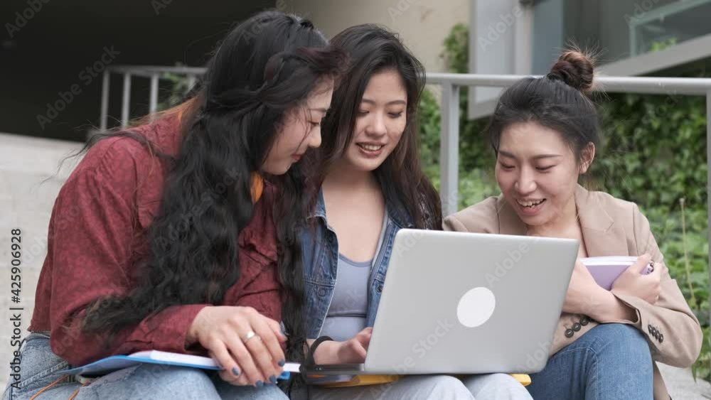 Group of Asian female students using a laptop and studying together while sitting on the stairs of the university campus. Group of Asian female students using a laptop and studying together while sitting on the stairs of the university campus.