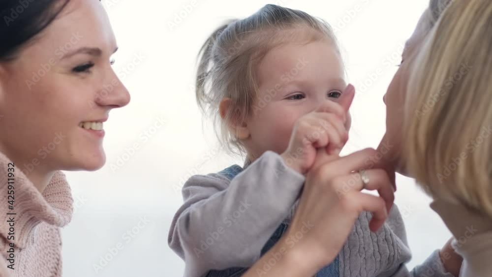 Two mothers and a young daughter spend time at home. They're playing on the window sill. Warm home clothes. Lgbt family, lesbians with a child. Two mothers and a young daughter spend time at home. They're playing on the window sill. Warm home clothes. Lgbt family, lesbians with a child.