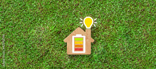 Energy efficiency and rating chart in a small model house with glowing lightbulb in the chimney over green grass in an ecological and environmental concept