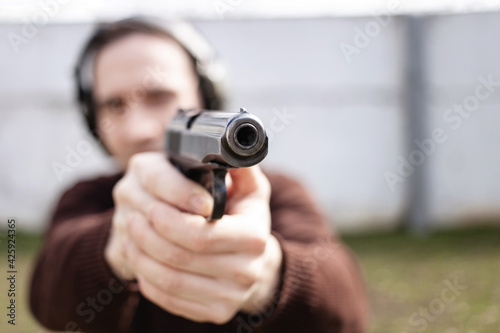 A man is aiming for a gun. A man wearing protective headphones. outdoor tyre shooting range. hobby. firearm against the white wall copy space