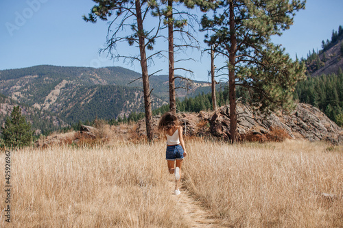 A young woman walks along a path among the dry grass. Beautiful landscape with mountains, forest and large rocks on a sunny day. Recreation Area, I-90, Alberton, Montana, USA 9-3-2020 photo