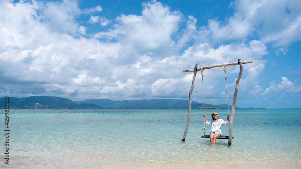 A beautiful young asian woman sitting on swing in the sea with blue sky background