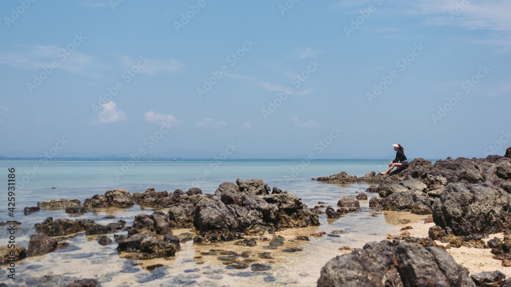 A young woman sitting on the rock by the sea