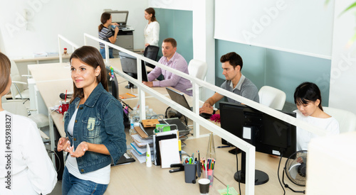 Glad smiling male and female office co-workers having conversation at desk in office