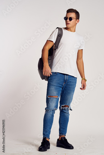 a man with a backpack on his back in jeans t-shirt full length sneakers and glasses on his face