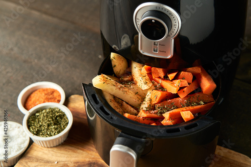 Cooking potatoes and carrot sticks with spices in an air fryer photo