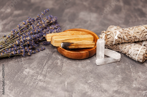 Balancing the soul.Cleansing kit, selenite stick. Magic crystals and rocks. Smudge kit for spiritual practices with natural elements: Palo Santo sticks, dried white sage, crystals on a grey background photo