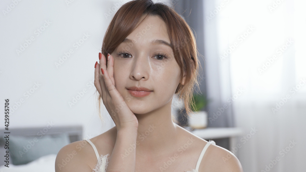 closeup smiling young korean lady looking at herself in the mirror hand feel her flawless skin softly after putting on day cream. anti-aging beauty routine concept.
