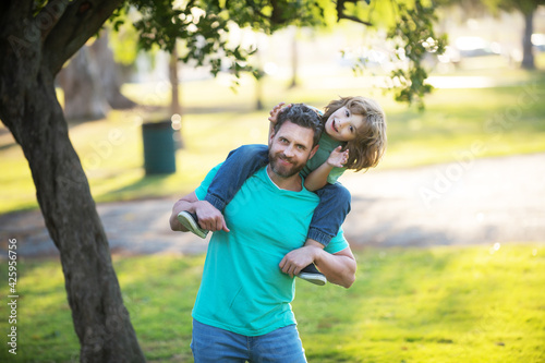 Father carrying son on shoulders outdoors. Portrait of a young dad and his child in the park.