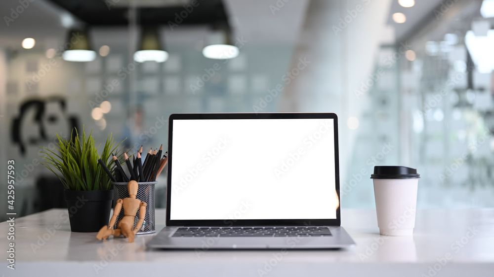 Fototapeta premium Front view of mock up computer laptop ehh empty screen, coffee cup, plant and pencil holder on white table.