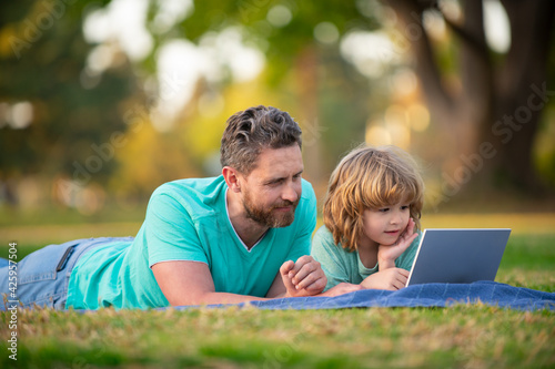 Blogging. Happy father using laptop relax with schooler son holding laptop. Childhood and parenthood kids concept. Video lesson. Happy father and son use notebook together outdoor. © Volodymyr