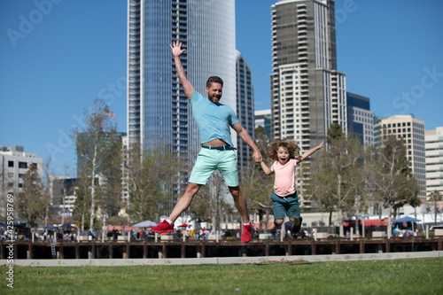 Funny father and son jumping in city background. Childhood and parenthood kids concept. Happy father and son playing together outdoor. Urban families.