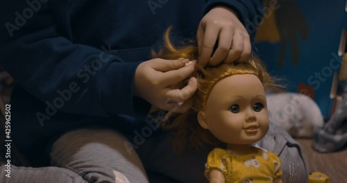 Little girl play with doll in home. Girl preschooler makes hairstyle doll.  
 photo