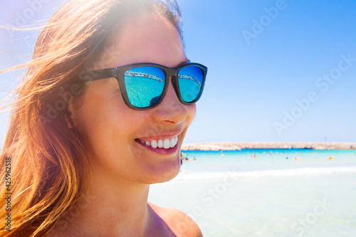 Summer fun vacation. Young and beautiful smiling woman with sunglasses. Blue sea in the background. Beach holiday. Sunbeam top