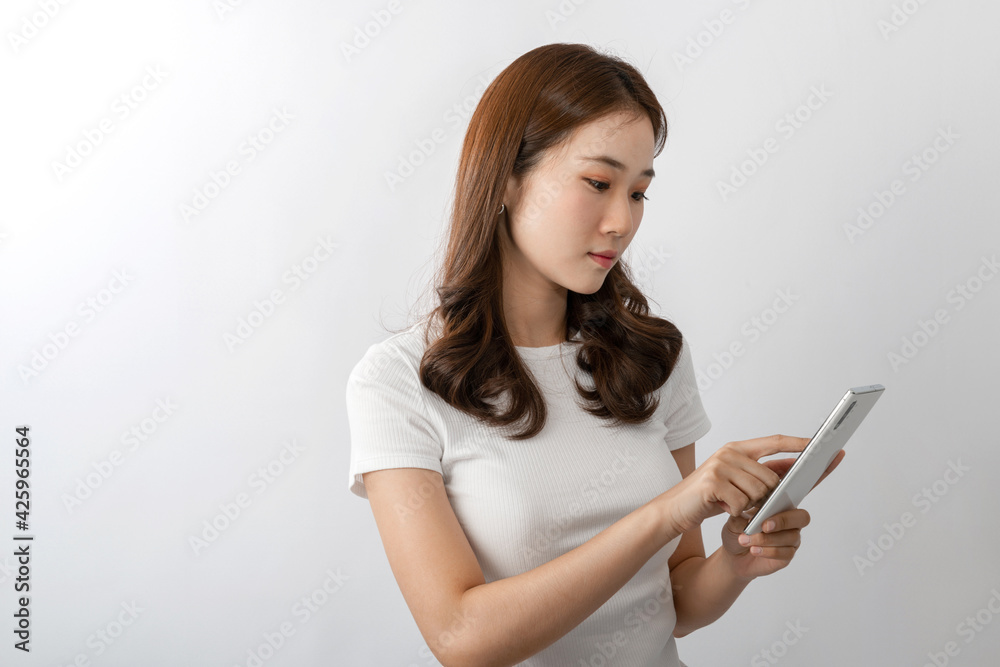 A young beautiful Asian woman with long hair smiling uses a cell phone for texting, chatting, or social media. On white background in A studio. Online technology, online shopping concept. Copy space A young beautiful Asian woman with long hair smiling uses a cell phone for texting, chatting, or social media. On white background in A studio. Online technology, online shopping concept. Copy space