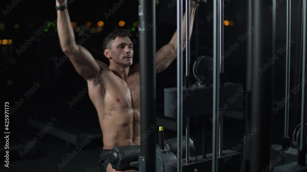 Athletic man in the gym lifting blocks on rack machine, training on block device and gym equipment, night time, 4k slow motion. Athletic man in the gym lifting blocks on rack machine, training on block device and gym equipment, night time, 4k slow motion.