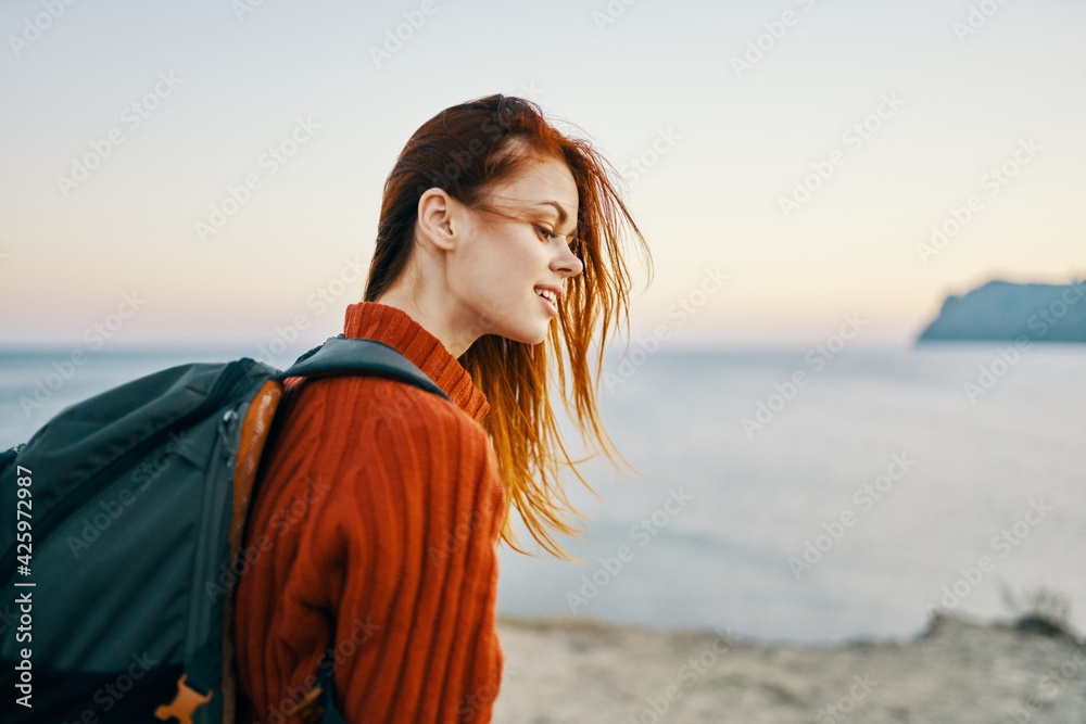 woman tourist with a backpack and in a red sweater walks on the beach near the sea in the mountains woman tourist with a backpack and in a red sweater walks on the beach near the sea in the mountains