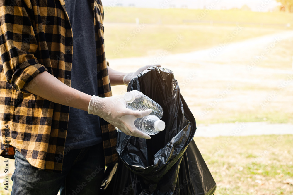 Man's hands pick up plastic bottles, put garbage in black garbage bags to clean up at parks, avoid pollution, be friendly to the environment and ecosystem Man's hands pick up plastic bottles, put garbage in black garbage bags to clean up at parks, avoid pollution, be friendly to the environment and ecosystem