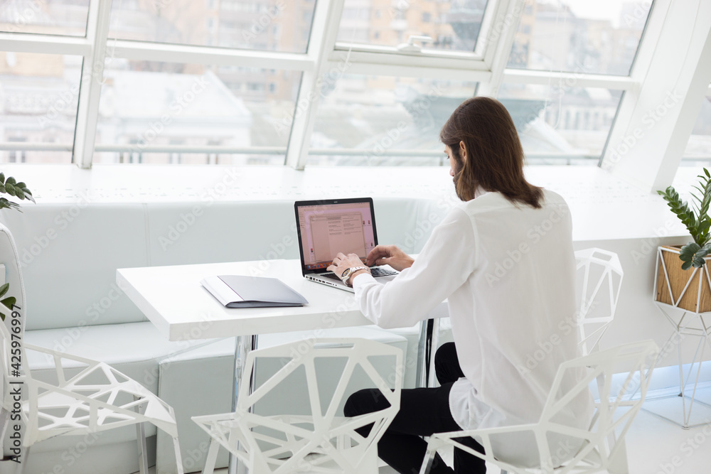 portrait of a business man in a white shirt and tie sits working with a laptop and documents in a modern expensive office by the window
portrait of a business man in a white shirt and tie sits working with a laptop and documents in a modern expensive office by the window