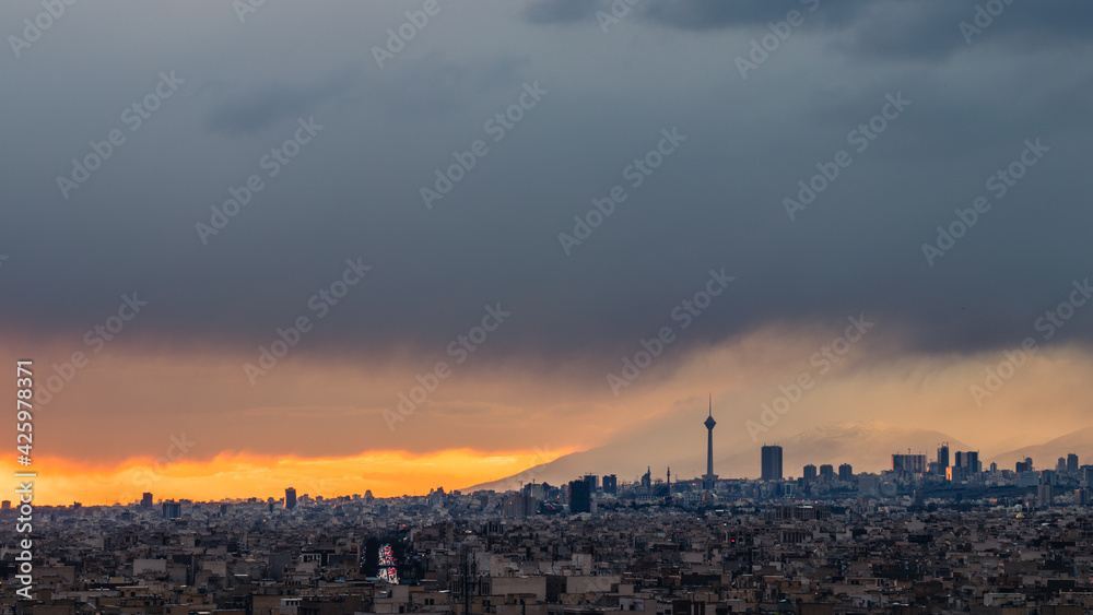Tehran-Iran skyline at a moody sunset after a heavy storm.
with Milad tower and beautiful snow covered mountains and amazing clouds in the background.