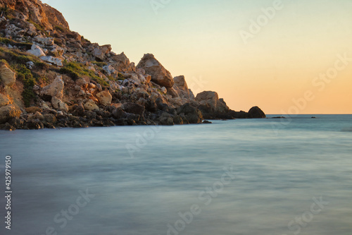 Orange sky over rocks and blue water at sunset at Golden Bay, Malta.