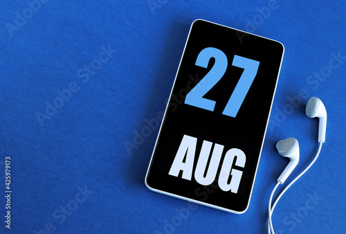 August 27. 27 st day of the month, calendar date. Smartphone and white headphones on a blue background. Place for your text. Summer month, day of the year concept