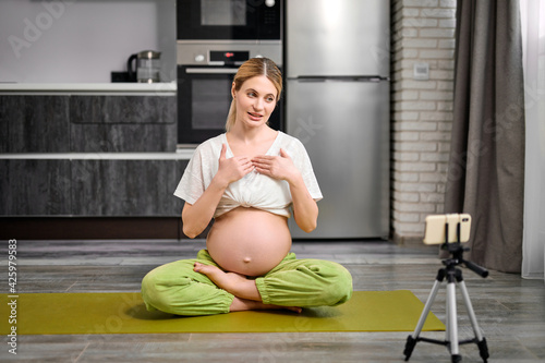 friendly pregnant female sit on fitness mat recording video on smartphone photo