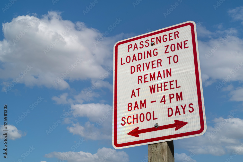 School Days Passenger Loading Zone, Driver to Remain at Wheel sign with white clouds and blue sky background School Days Passenger Loading Zone, Driver to Remain at Wheel sign with white clouds and blue sky background