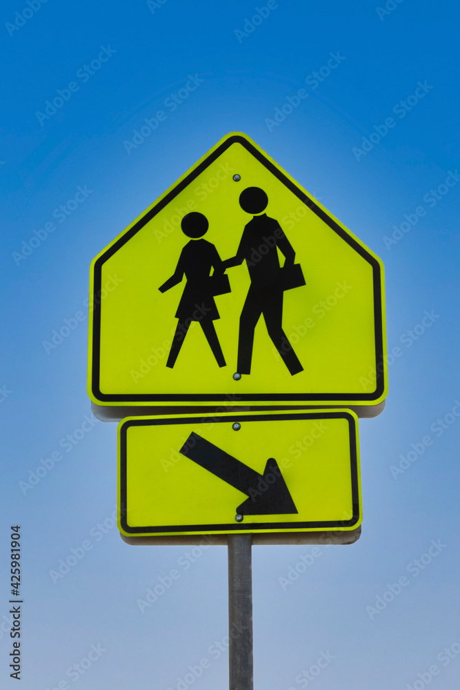 Bright yellow and black pedestrian crosswalk sign with a figure of a man and woman with a clear blue sky background Bright yellow and black pedestrian crosswalk sign with a figure of a man and woman with a clear blue sky background