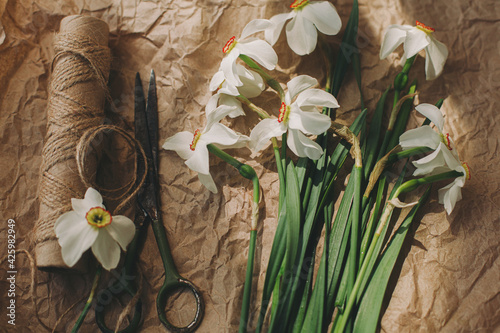 Stylish spring flowers rural still life. Daffodils, scissors, twine in sunny light on rustic paper