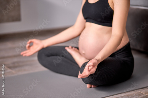 Young Pregnant Woman Meditating On Floor At Home, With Crossed Legs