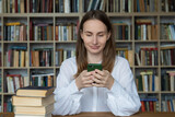Woman student sitting at a desk and using a smartphone in the library