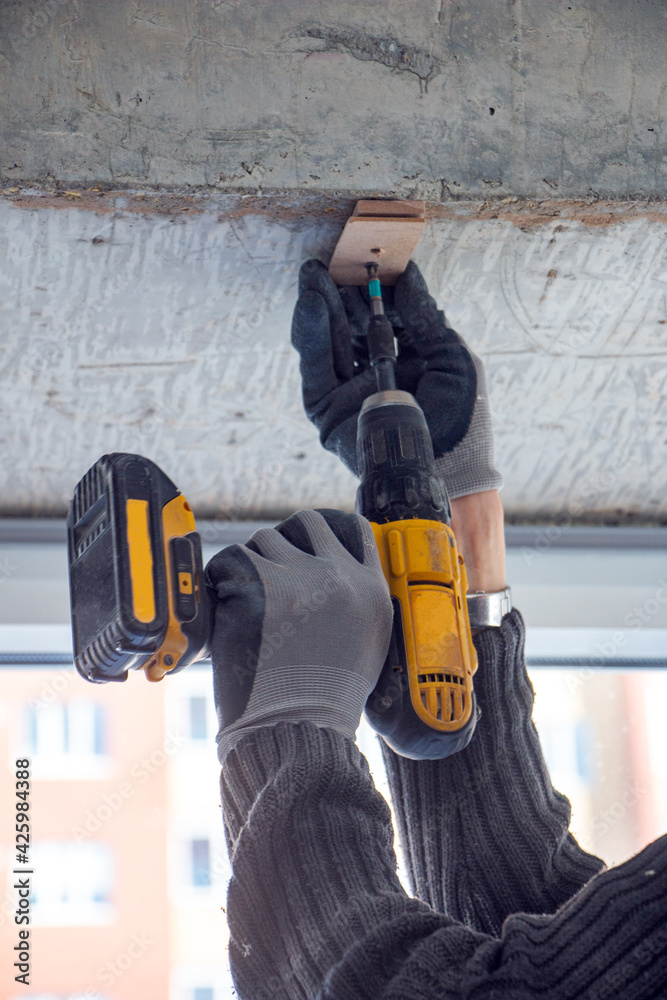 male hands of  construction worker tighten and fix  screws and self-tapping screw  with  electric cordless screwdriver for home improvement and building interior decoration.