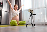 calm caucasian pregnant woman sit doing exercises on floor and recording video