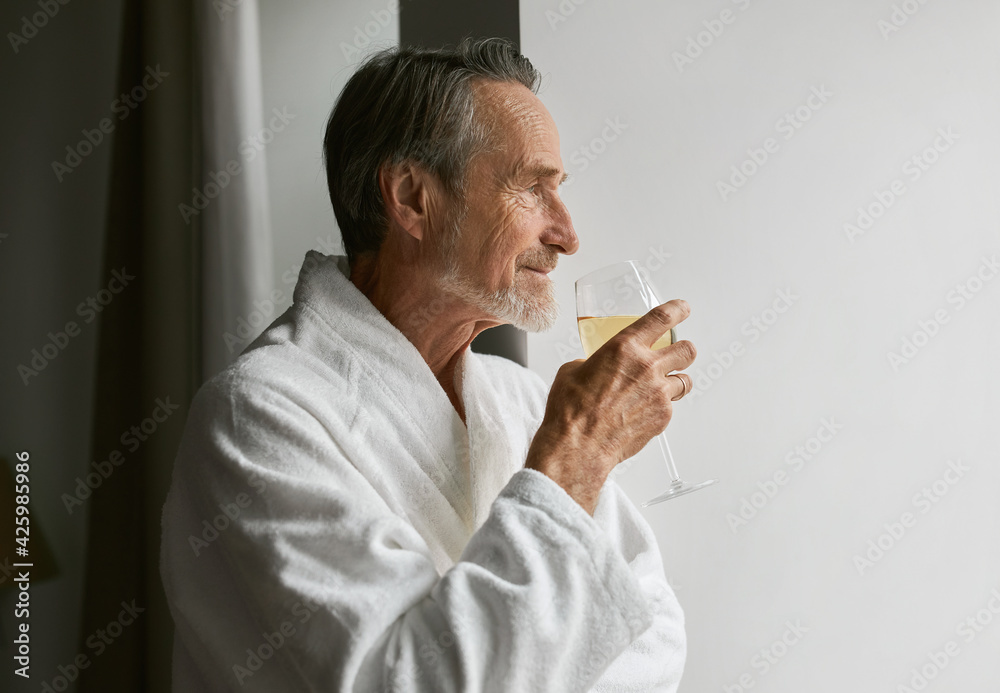 Side view of a caucasian bearded man holding a glass wine wearing bathrobe at hotel room Side view of a caucasian bearded man holding a glass wine wearing bathrobe at hotel room