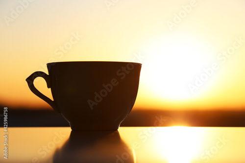 Silhouette of coffee cup on sunrise background, fresh start in the morning. Cozy atmosphere, city view from the window