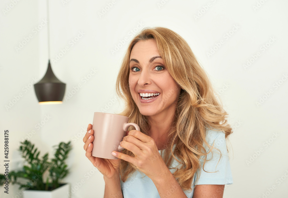 A portrait of a beautiful middle-aged smiling woman on a self-isolation with a cup. A portrait of a beautiful middle-aged smiling woman on a self-isolation with a cup.