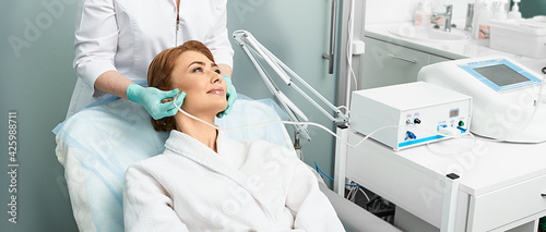 Adult woman getting rejuvenation skin face with ozone therapy procedure at beauty clinic using oxygen skin care machine photo