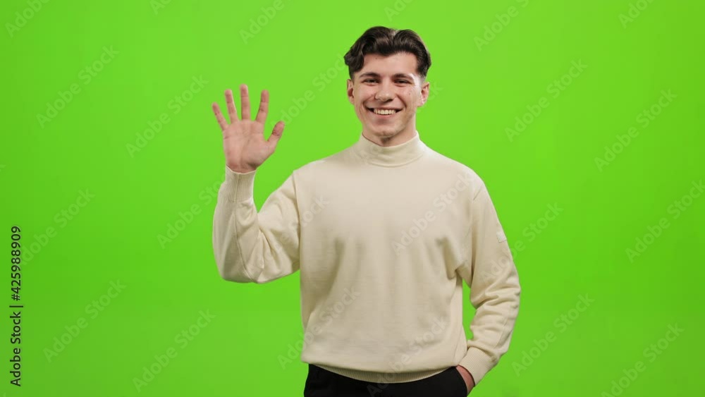 The man is standing and looking at the camera. He raising his hand and waving hello. He is laughing. He is standing on a green background. Green screen. 4K The man is standing and looking at the camera. He raising his hand and waving hello. He is laughing. He is standing on a green background. Green screen. 4K