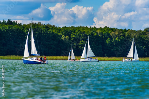 Fototapeta Naklejka Na Ścianę i Meble -  Yacht sailing on the lake against a blue sky with clouds. Sailboat vacations on a lake.