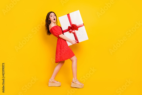 Full size profile photo of impressed girl arms hold big heavy giftbox open mouth isolated on yellow color background