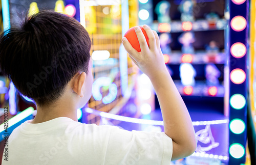 Kid boy playing a game of darts,holding a small plastic ball in his hands,aiming throwing at a target or a toy doll to knock it down,little child hurl the ball at the toys placed on the shelf to fall