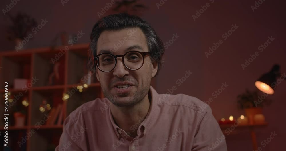 Crop view of cheerful male person talking and making heart sign with hands while looking to camera. Smiling man in glasses blowing kisses and communicating online while sitting at home.