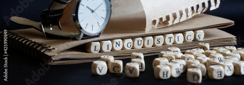 Wristwatch, eco-friendly notepad and the word linguistics made of wooden cubes on a dark. Concept for scientific research in linguistics and teaching at school or college photo