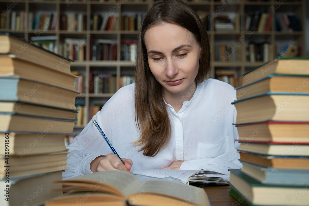 Female student sits at a table in the library, littered with books. Female student sits at a table in the library, littered with books.