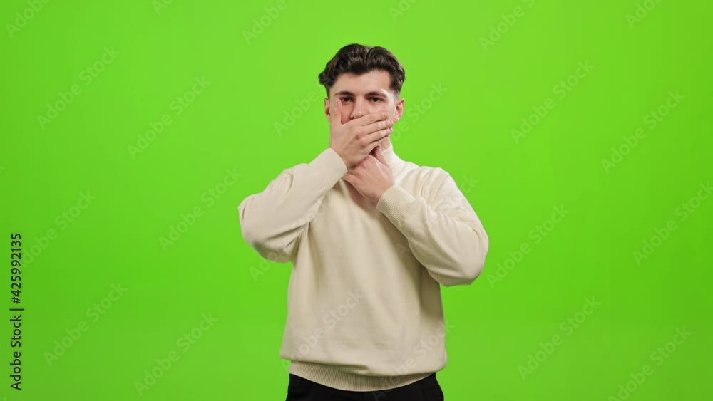 The man is standing and looking at the camera. He is covering his ears, mouth, and eyes with his hands. He is standing on a green background. Green screen. 4K The man is standing and looking at the camera. He is covering his ears, mouth, and eyes with his hands. He is standing on a green background. Green screen. 4K