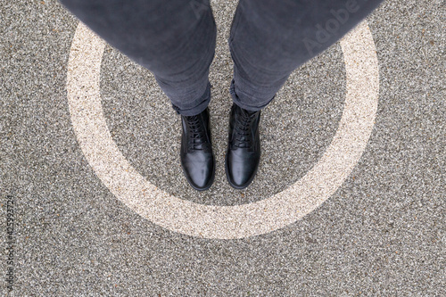 Black shoes standing in white circle on the asphalt concrete floor. Comfort zone or frame concept. Feet standing inside protected area zone circle. Place for text, banner