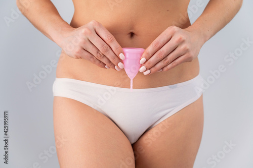 Close-up of a woman in white cotton panties holding a pink menstrual cup against a white background. Alternative to tampons and pads