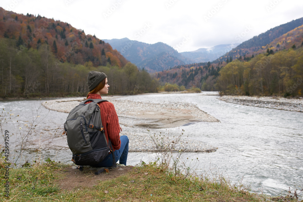 Fototapeta premium traveler sits on the banks of the river in the mountains in nature back view