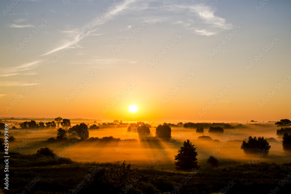 sunrise on a foggy field, the first rays of the sun through the fog, the beauty of a red sunset